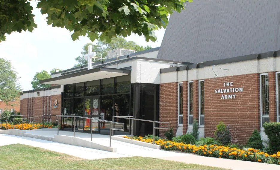 The front entrance of The Salvation Army Burlington Community Church at 2090 Prospect Street, a brick building with a white cross above the doors and marigolds in bloom along the walkway.